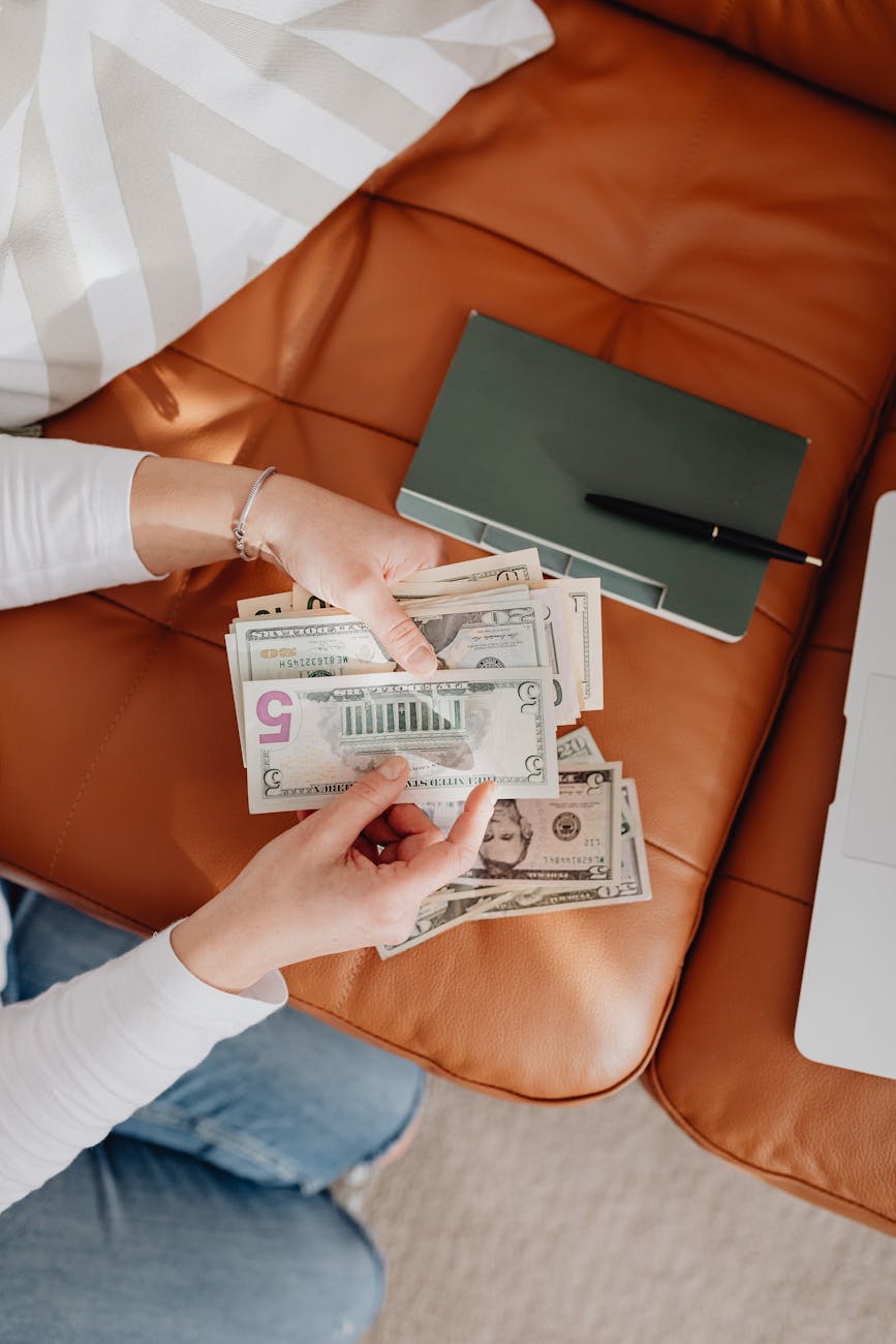 top view of woman counting money and notebook on leather sofa