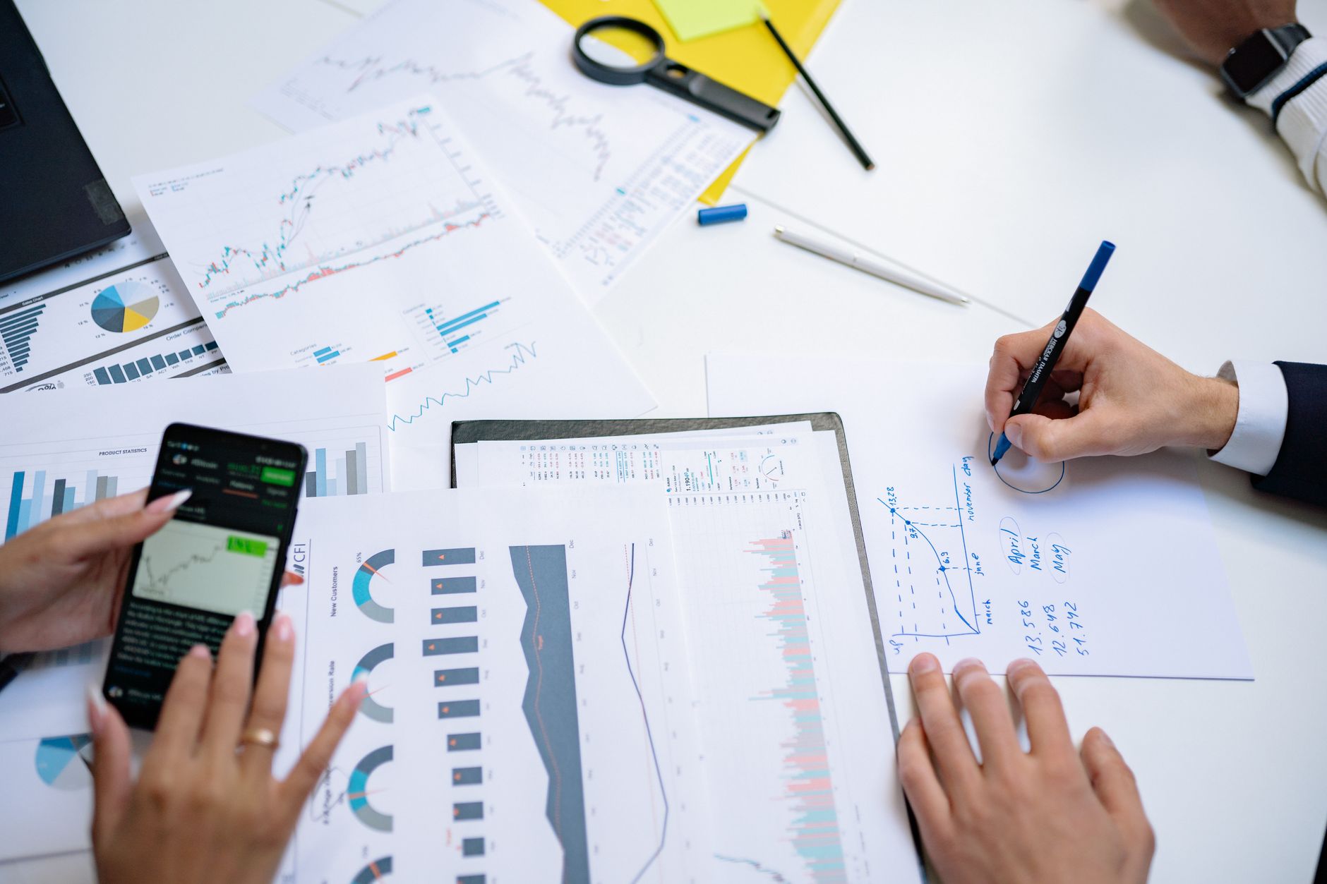hands holding smartphone and writing on table with charts at office